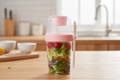Portable salad container with pink lid, dressing compartment and fork, filled with fresh salad